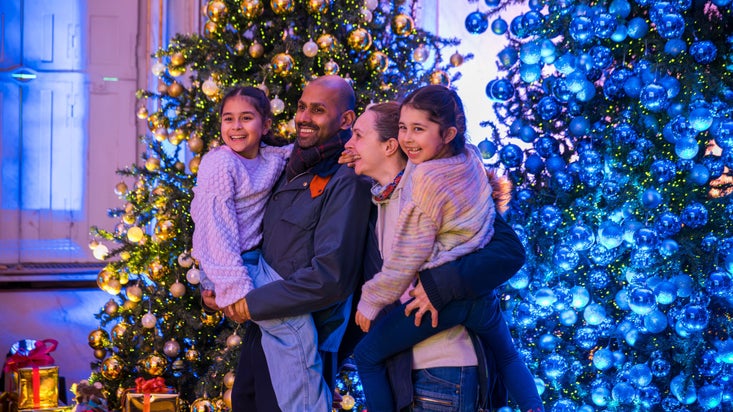 Man and woman both holding a young girl, standing smiling into the distance in Mottisfont's dining room, with decorated Christmas trees in backgroune